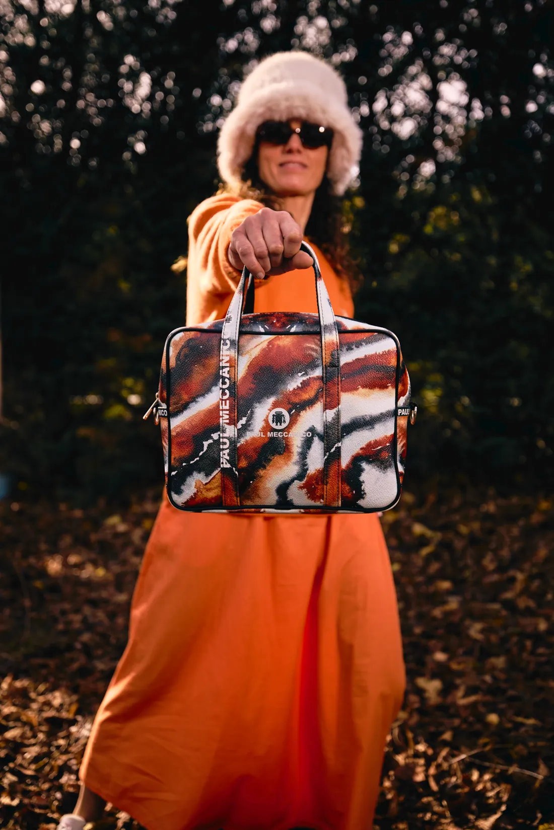 Une femme en robe orange et chapeau de fourrure tenant un sac Paul Meccanico coloré